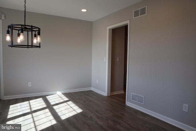 spare room with dark wood-type flooring and a chandelier