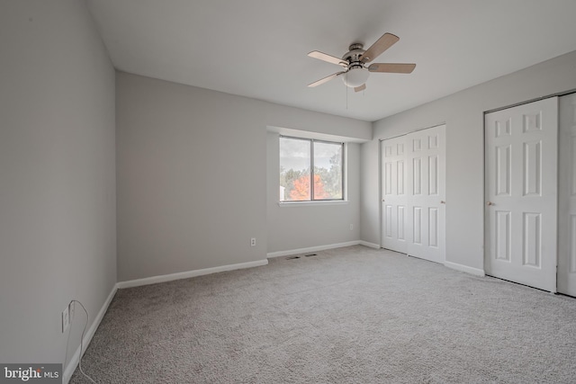 unfurnished bedroom featuring multiple closets, light colored carpet, and ceiling fan