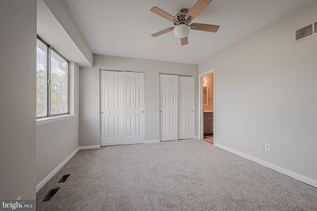 unfurnished bedroom with multiple closets, ensuite bathroom, carpet floors, and ceiling fan