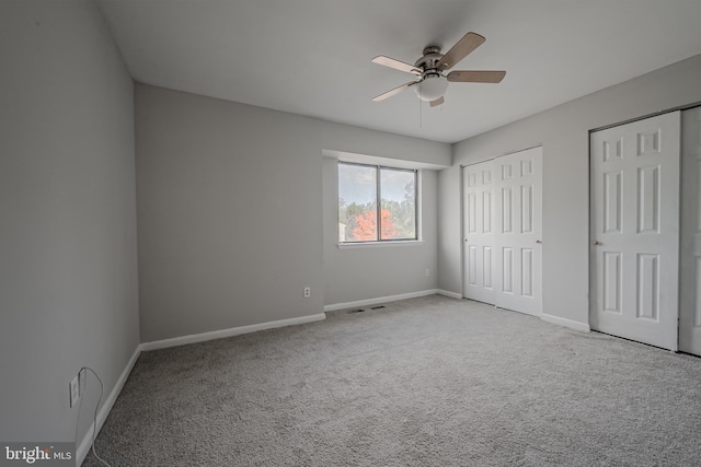 unfurnished bedroom with light carpet, two closets, and ceiling fan