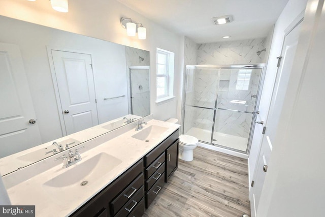 full bath with a marble finish shower, double vanity, wood finished floors, and a sink