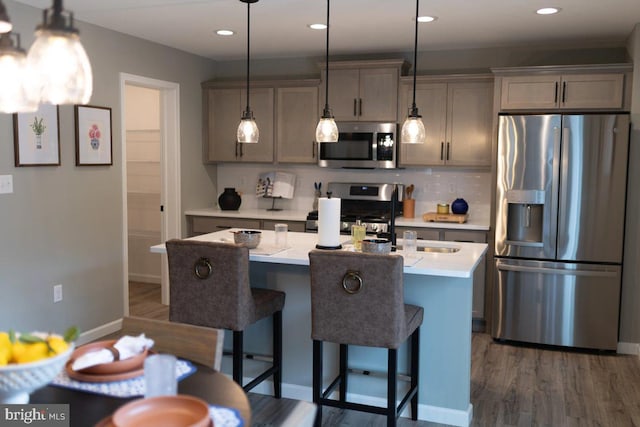 kitchen with appliances with stainless steel finishes, dark hardwood / wood-style flooring, gray cabinetry, a kitchen island with sink, and pendant lighting