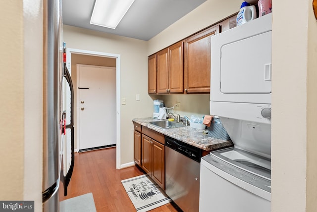 kitchen with light hardwood / wood-style floors, sink, stainless steel appliances, and stacked washer and clothes dryer