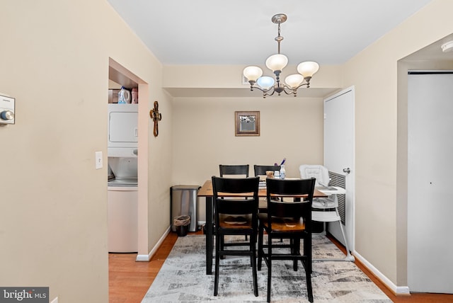 dining area with stacked washer and dryer, light hardwood / wood-style floors, and an inviting chandelier