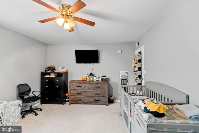 bedroom with ceiling fan, light carpet, and a nursery area