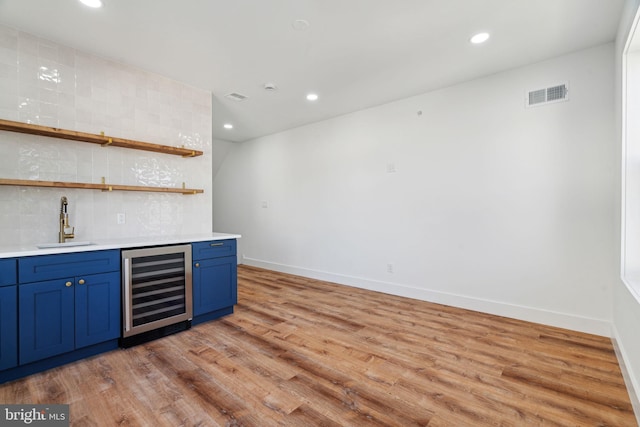 bar with blue cabinetry, beverage cooler, sink, and light wood-type flooring