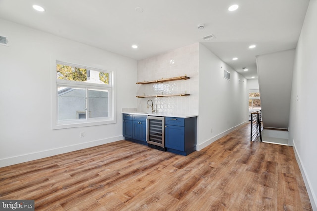 bar with decorative backsplash, light hardwood / wood-style floors, blue cabinets, and wine cooler