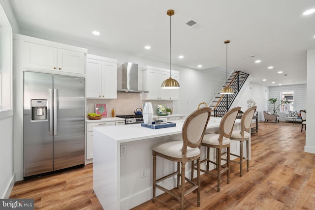 kitchen featuring light wood-type flooring, wall chimney exhaust hood, decorative light fixtures, and appliances with stainless steel finishes