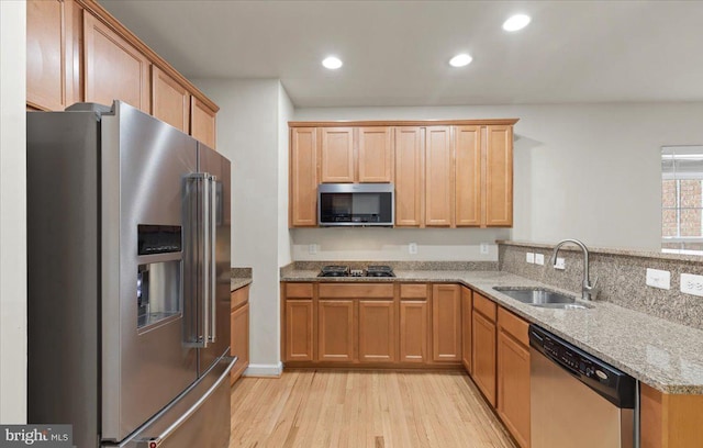 kitchen with sink, appliances with stainless steel finishes, light hardwood / wood-style floors, light stone counters, and kitchen peninsula