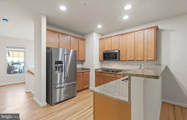 kitchen featuring kitchen peninsula, stainless steel appliances, light stone countertops, and light hardwood / wood-style floors