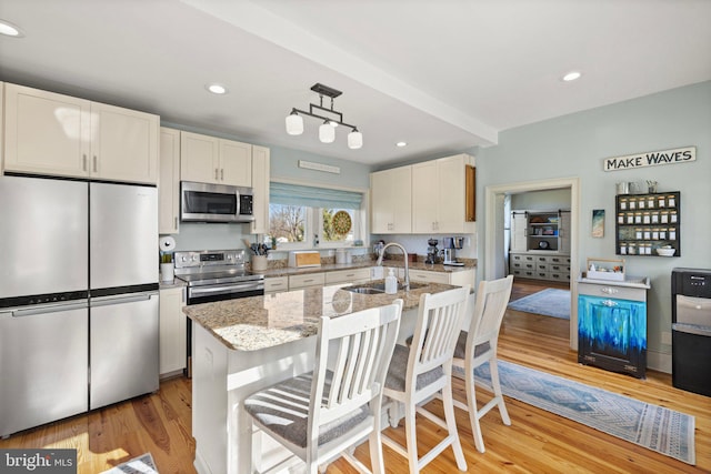 kitchen featuring a center island with sink, light hardwood / wood-style flooring, sink, pendant lighting, and appliances with stainless steel finishes