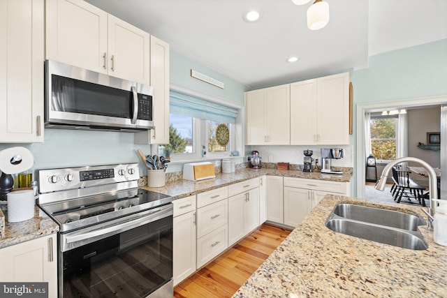 kitchen with stainless steel appliances, sink, light stone countertops, white cabinetry, and light hardwood / wood-style flooring