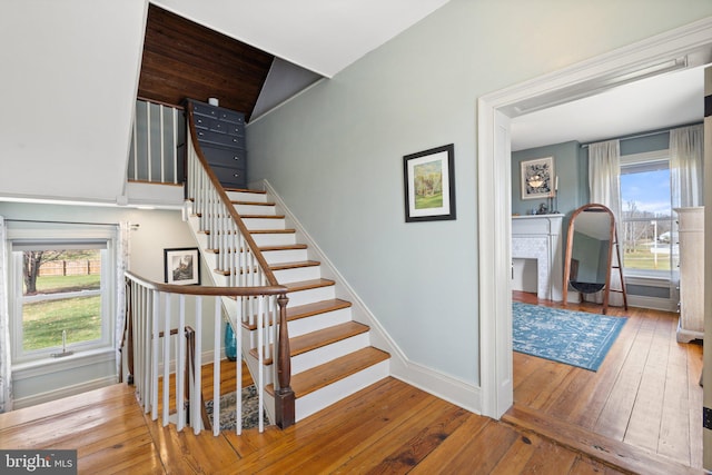 staircase with wood-type flooring, a healthy amount of sunlight, and vaulted ceiling