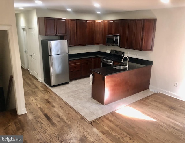 kitchen with sink, dark brown cabinets, kitchen peninsula, stainless steel appliances, and light hardwood / wood-style flooring