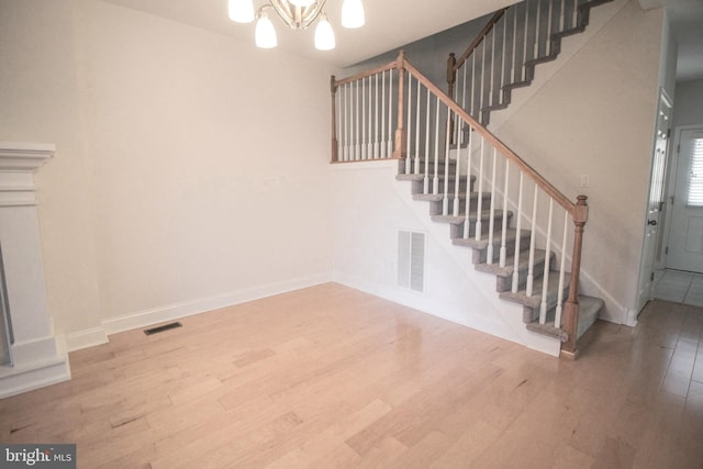 stairs featuring wood-type flooring and an inviting chandelier