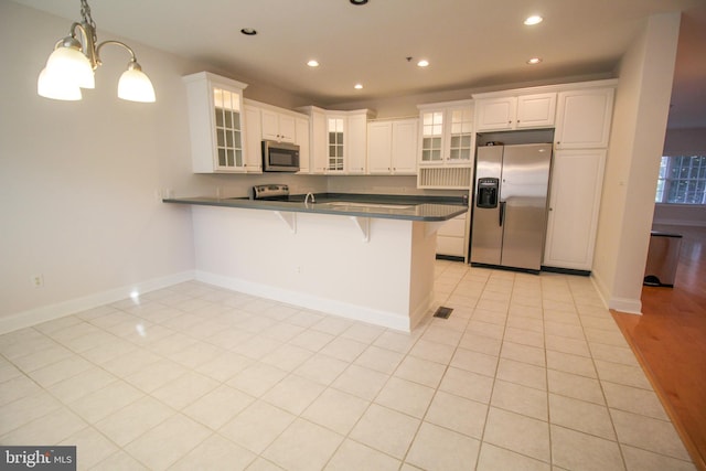 kitchen with white cabinets, appliances with stainless steel finishes, decorative light fixtures, a kitchen breakfast bar, and kitchen peninsula