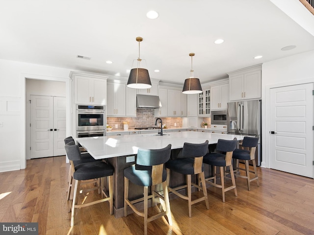 kitchen featuring pendant lighting, appliances with stainless steel finishes, a large island with sink, and light hardwood / wood-style flooring