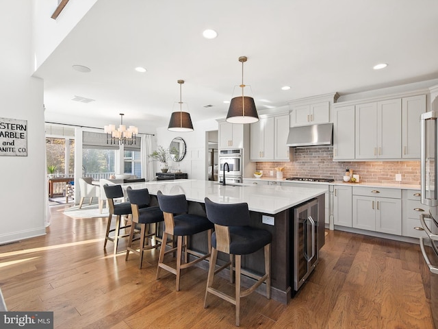 kitchen featuring hardwood / wood-style floors, a large island with sink, decorative light fixtures, and wine cooler