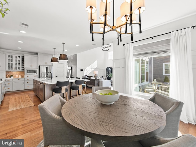 dining area featuring an inviting chandelier, sink, and light hardwood / wood-style flooring