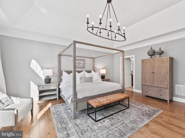 bedroom featuring hardwood / wood-style flooring, crown molding, and a notable chandelier