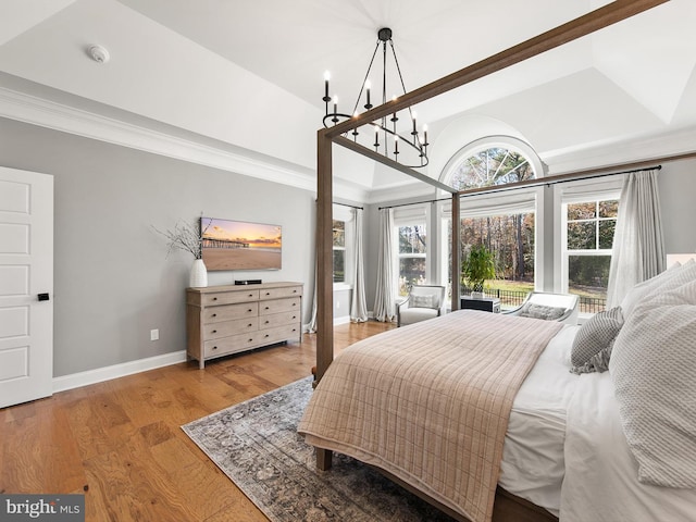 bedroom with a tray ceiling, multiple windows, an inviting chandelier, and light hardwood / wood-style flooring