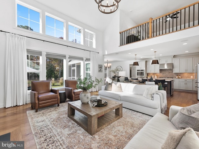 living room with a chandelier, light wood-type flooring, a wealth of natural light, and a towering ceiling