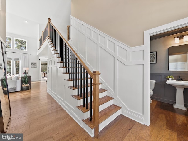 stairway with a towering ceiling, wood-type flooring, and sink