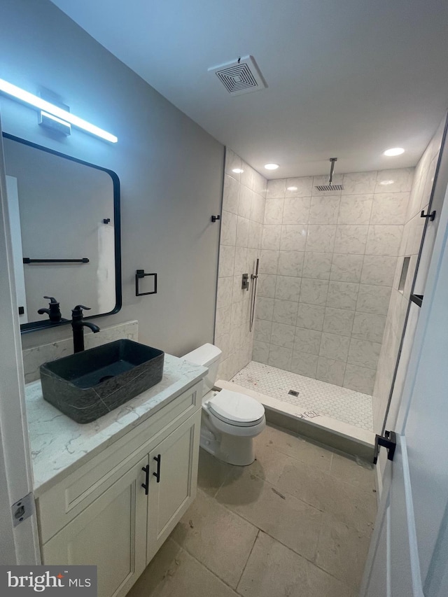 bathroom with a tile shower, vanity, tile patterned floors, and toilet