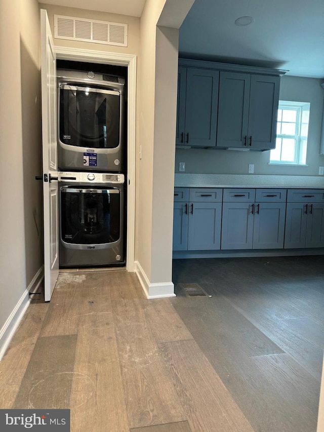 laundry room with stacked washing maching and dryer and light hardwood / wood-style floors