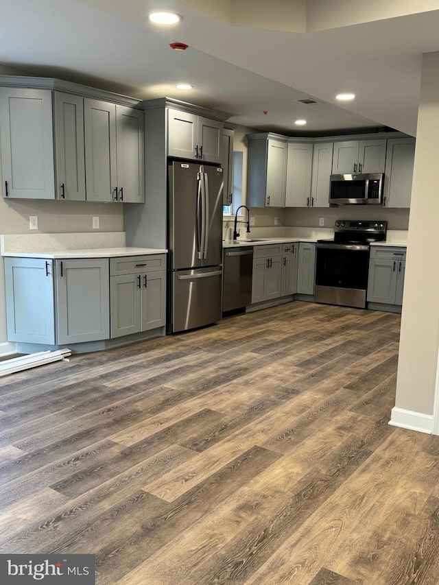 kitchen with appliances with stainless steel finishes, dark wood-type flooring, sink, and gray cabinetry