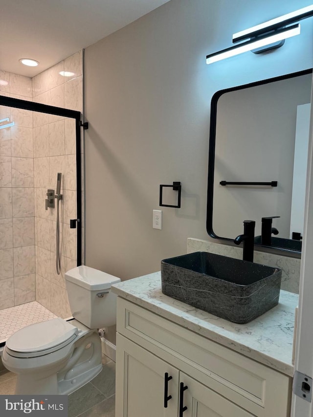 bathroom featuring toilet, vanity, tile patterned flooring, and a tile shower