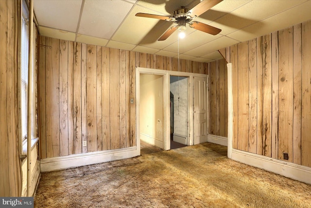 carpeted spare room featuring a drop ceiling, wooden walls, and ceiling fan