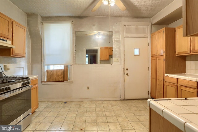 kitchen with tile counters, ceiling fan, stainless steel gas stove, and light tile patterned floors