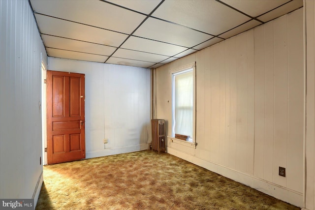 empty room featuring wood walls, carpet, a drop ceiling, and radiator heating unit