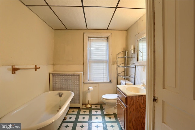 bathroom with a bathing tub, radiator, toilet, vanity, and a drop ceiling