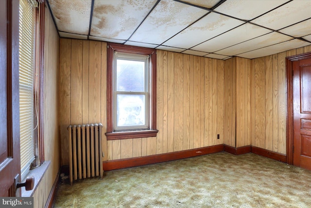 carpeted spare room featuring wood walls, radiator, and a paneled ceiling