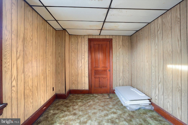 carpeted empty room featuring wood walls and a drop ceiling