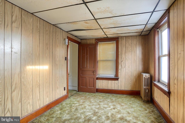 carpeted spare room featuring radiator, wood walls, and a drop ceiling