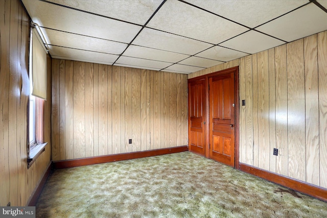 unfurnished room featuring a paneled ceiling, wooden walls, and carpet flooring