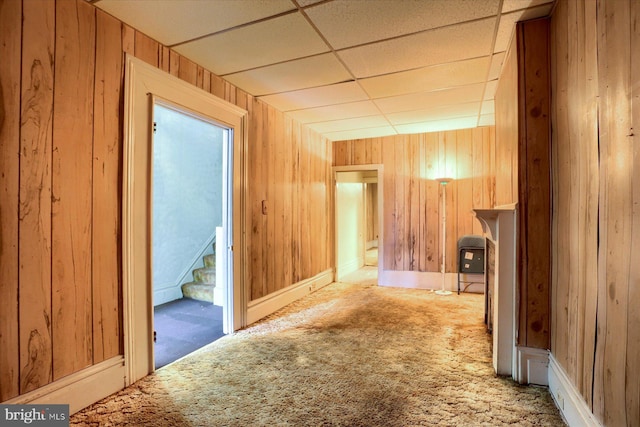 hallway featuring carpet floors, wooden walls, and a paneled ceiling