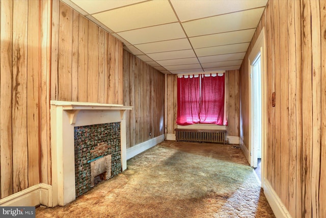 unfurnished living room featuring a drop ceiling, radiator heating unit, wood walls, and carpet floors