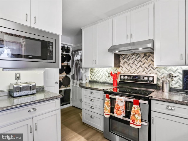 kitchen with white cabinetry, backsplash, dark stone counters, appliances with stainless steel finishes, and hardwood / wood-style flooring