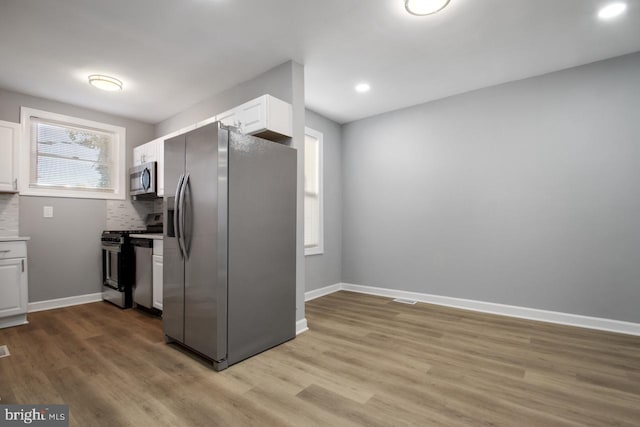 kitchen with white cabinetry, stainless steel appliances, light hardwood / wood-style floors, and tasteful backsplash