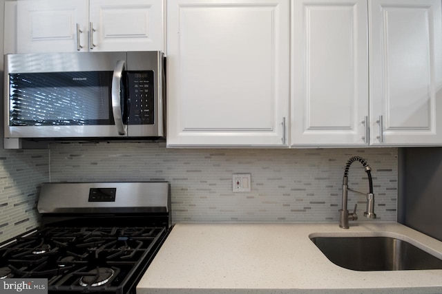 kitchen with black range with gas stovetop, white cabinetry, sink, and decorative backsplash