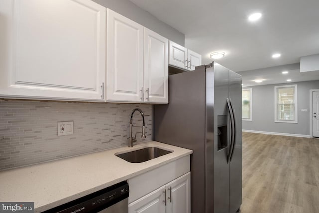 kitchen featuring sink, backsplash, stainless steel appliances, white cabinets, and light hardwood / wood-style flooring