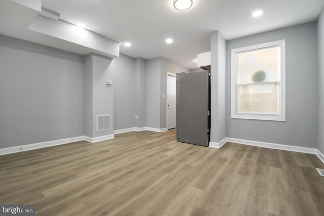 basement featuring light hardwood / wood-style flooring and stainless steel refrigerator