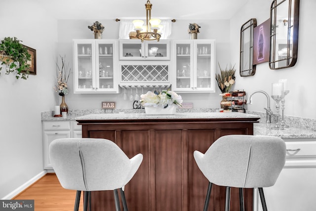 bar with white cabinetry, hanging light fixtures, light stone counters, and light wood-type flooring