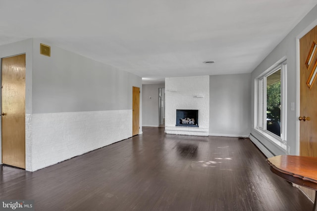 unfurnished living room featuring dark hardwood / wood-style floors, baseboard heating, and a brick fireplace