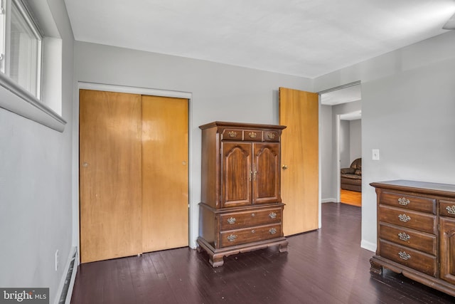 bedroom with a closet, a baseboard heating unit, and wood-type flooring