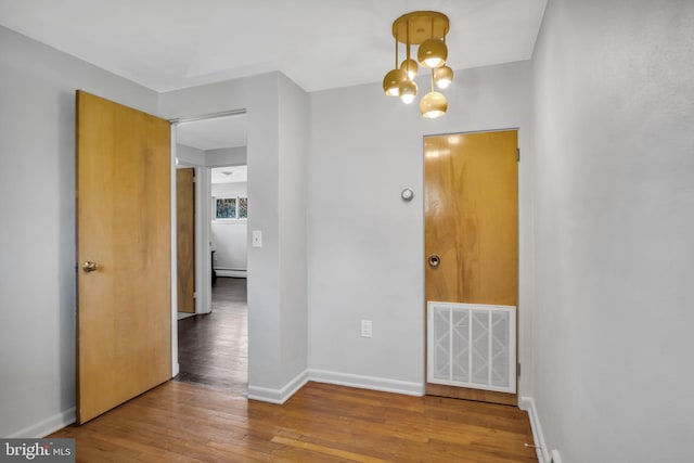 spare room featuring a baseboard radiator, hardwood / wood-style flooring, and an inviting chandelier